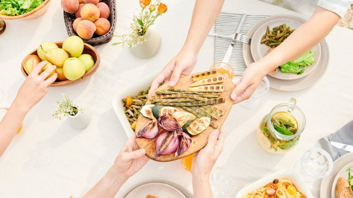 Overhead view of a family sharing a meal with fresh grilled vegetables and fruits, perfect for a healthy lifestyle.